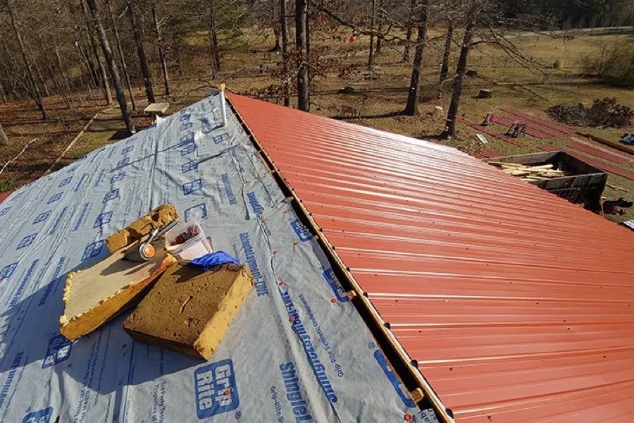 Red metal roof panels being installed over synthetic underlayment